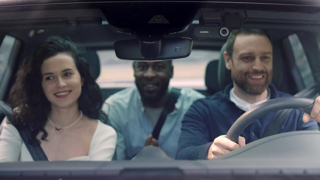 Three smiling passengers in a car with a DDPAI dashcam installed